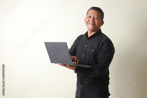 Asian mature man looking at the camera while holding a laptop and showing a very happy expression photo