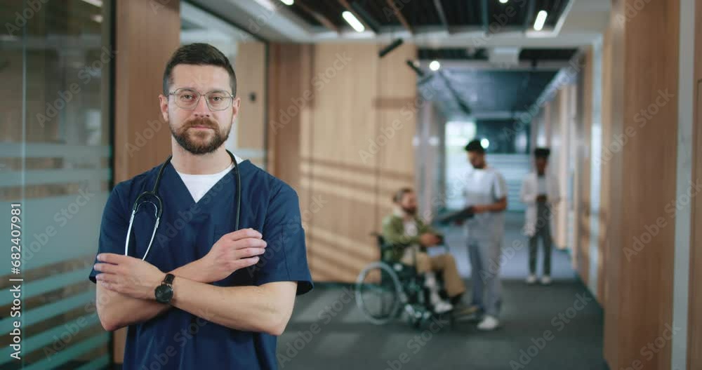 Portrait of attractive successful Caucasian doctor in uniform with stethoscope looking at camera and smiling. Happy professional medical worker standing at corridor with patient on background. Portrait of attractive successful Caucasian doctor in uniform with stethoscope looking at camera and smiling. Happy professional medical worker standing at corridor with patient on background.