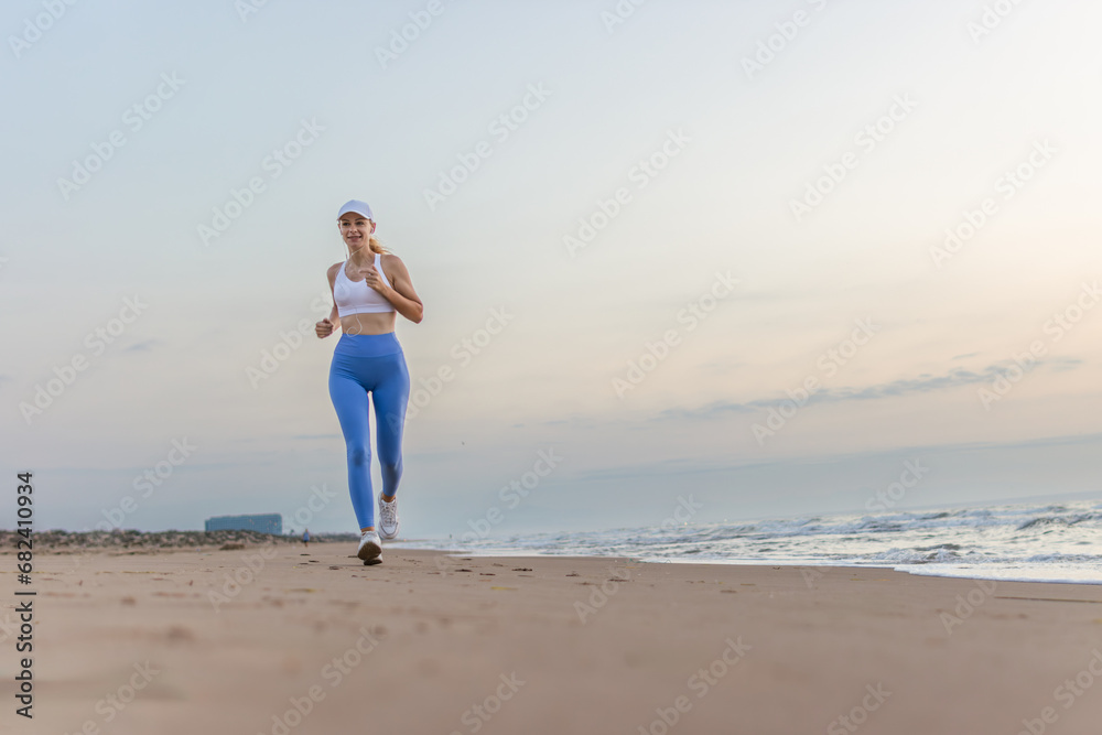 Beautiful sportive woman running along beautiful sandy beach enjoying active summer near the sea