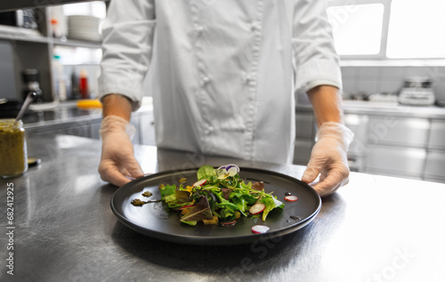 food cooking, profession and people concept - close up of male chef cook with plate of salad at restaurant kitchen table