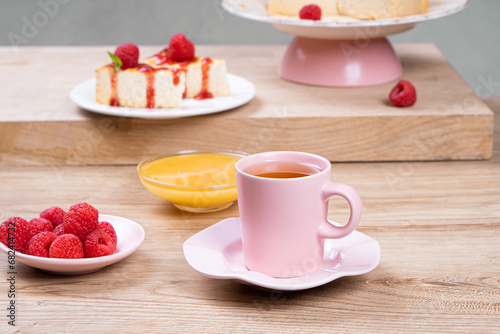 Colorful breakfast. Tea in a pink mug and dessert with raspberries on a light wooden table