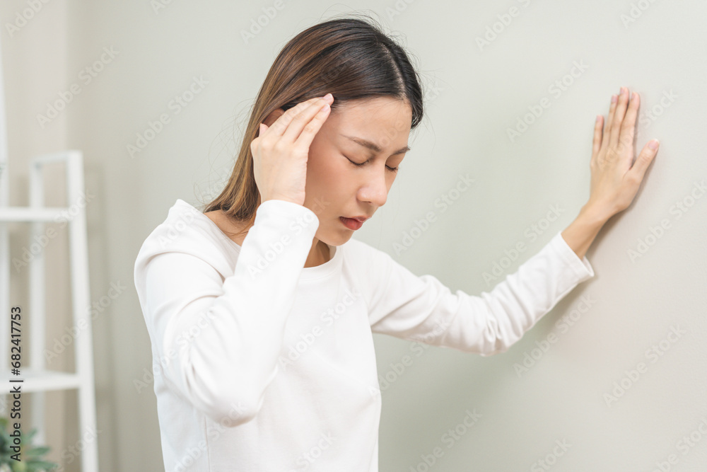 Dizzy asian young woman, girl headache or migraine pain. suffering from vertigo, difficulty standing up leaning on wall at home, holding head with hand, health problem of brain, inner ear not balance. Dizzy asian young woman, girl headache or migraine pain. suffering from vertigo, difficulty standing up leaning on wall at home, holding head with hand, health problem of brain, inner ear not balance.