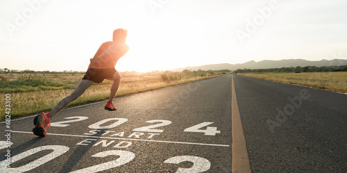 New year 2023 or start straight concept.word 2023 written on the asphalt road and athlete man runner stretching leg preparing for new year at sunset.Concept of challenge or career path and change.