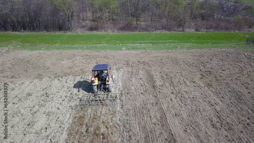 Obraz premium A farmer on a tractor with a seeder sows grain in plowed land in a private field in the village area. Mechanization of spring field work. Farmer's everyday life. Processing of land. The agrarian