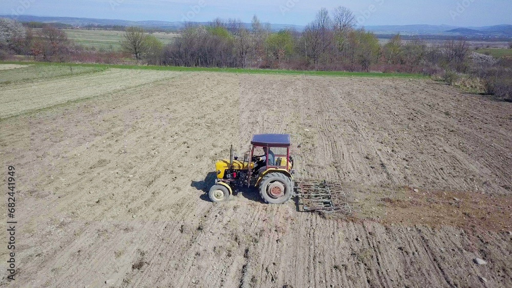 Obraz premium A farmer on a tractor with a seeder sows grain in plowed land in a private field in the village area. Mechanization of spring field work. Farmer's everyday life. Processing of land. The agrarian