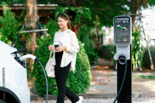 Young woman and sustainable urban commute with EV electric car recharging at outdoor cafe in springtime garden, green city sustainability and environmental friendly EV car. Expedient photo