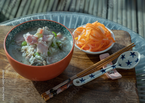 Hot Boiled rice or Rice porridge with Pork spare ribs soup and Ham served with Pickled carrot and Radish on Wooden cutting board. Healthy breakfast food, Space for text, Selective Focus.