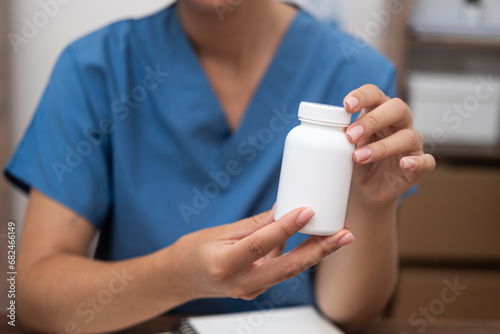close up pharmacist In a clinic setting, doctor, dressed in blue, holding a jar of pills while discussing treatment. 