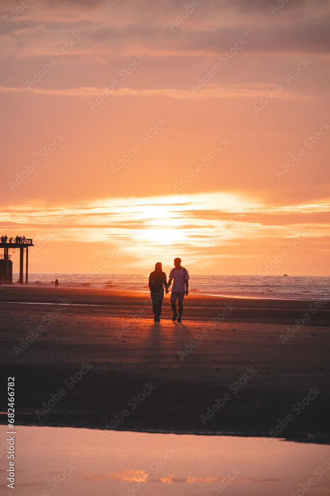 Romantic walk of a young couple on the beaches of Oostende in western Belgium at sunset. Love and devotion. Reflection in a pool of water