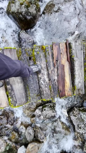 Slow motion 4K video POV view of Man's legs in trekking boots crossing mountain creek by wooden bridge during Makalu Barun National Park trek in Nepal. Mountain hiking and active people concept image. photo