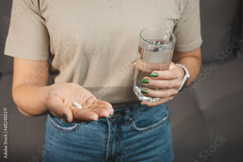 Young woman takes a medicine, white pill and holds in a hand glass of water, close-up view