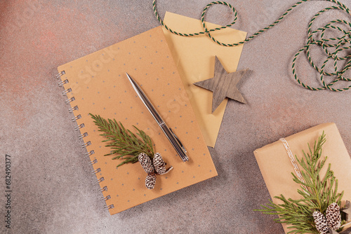Winter holiday mood, Christmas, New Year composition on gray background. Notebook with envelope and pen, handmade gift box and Christmas wooden decor. Flat lay, top view