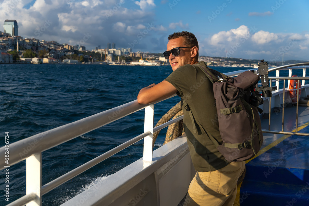Obraz premium Happy young male tourist with a backpack enjoys the sea and the city from a ferry in Istanbul on a sunny day. Concept of travel, tourism