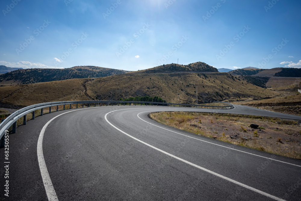 Fototapeta premium The desolate, empty and inviting highway stretching serpentine across the steppe. It is said that distance first accumulates inside a person, then it is only the road . Kars, Turkey.