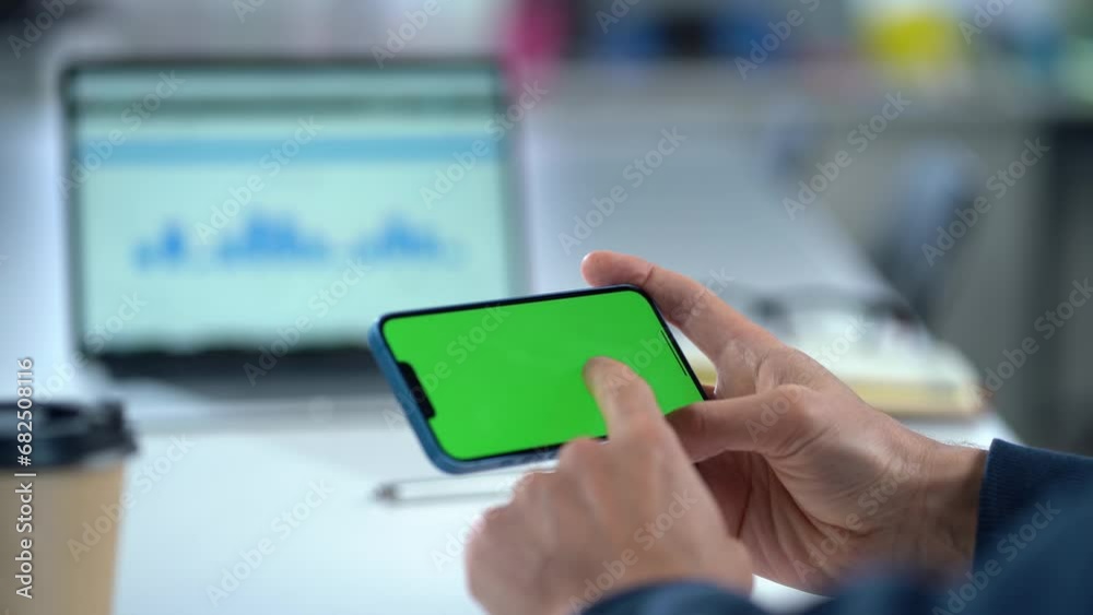 Close-up Of Mobile Phone With Green Mock-up Screen In Men's Hands On Desktop Background. Man Using Smartphone, Browsing Internet, Social Networks, Financial Reports Close-up Of Mobile Phone With Green Mock-up Screen In Men's Hands On Desktop Background. Man Using Smartphone, Browsing Internet, Social Networks, Financial Reports