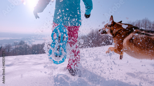 CLOSE UP, LOW ANGLE VIEW: Lady and her playful dog have fun running in snow