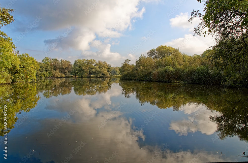 Bäume, Wolken und Himmel spiegeln sich in einem See 
Trees, clouds and sky are reflected in a lake