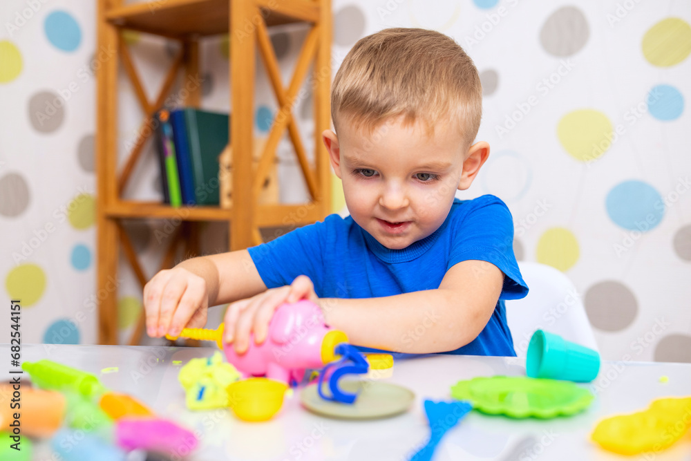 Little boy enthusiastically plays with plasticine, play dough on white table Little boy enthusiastically plays with plasticine, play dough on white table