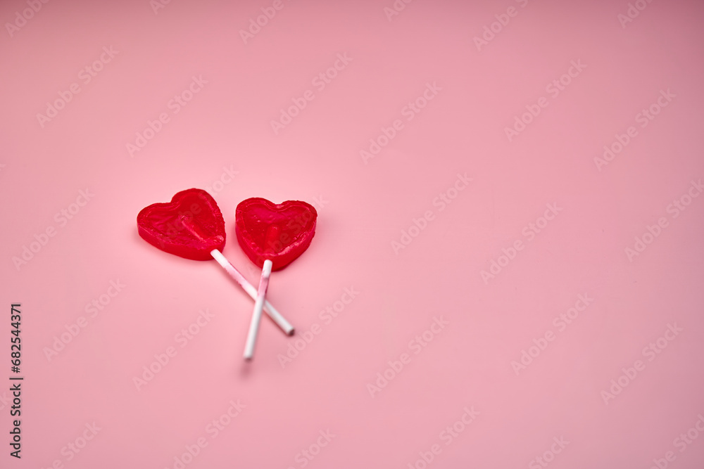 Representation of love through two heart-shaped lollipops on a pink background.