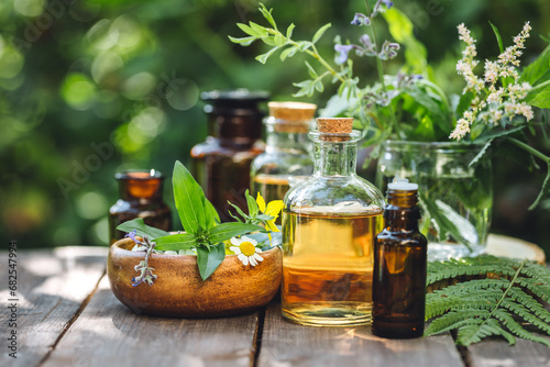 Herbal pure natural cosmetic ingredients on wooden background. Mix of holistic flowers and herbs, salt, massage herb-infused essential oil in glass bottles. Aromatherapy, fragrance production photo