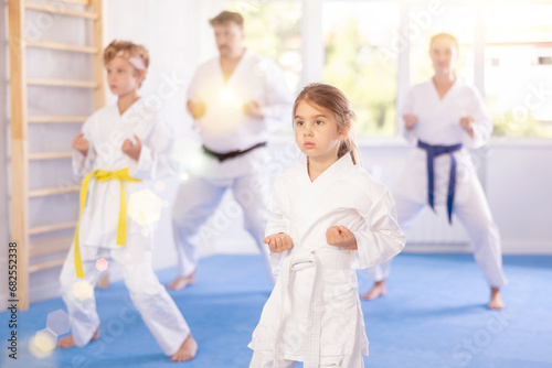 In gym, family of four repeats movements of karate card and practicing kicks and punches in unison, is intently preparing for sparring.