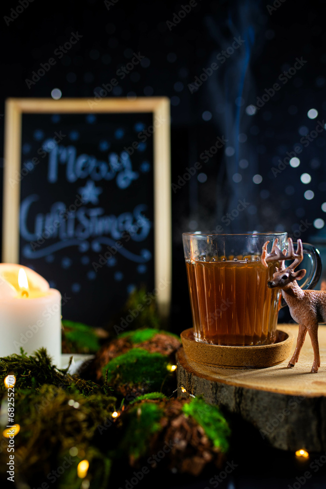 Christmas still life with hot tea cup, blackboard and deer figurine in candle lit setting. Vertical shot.