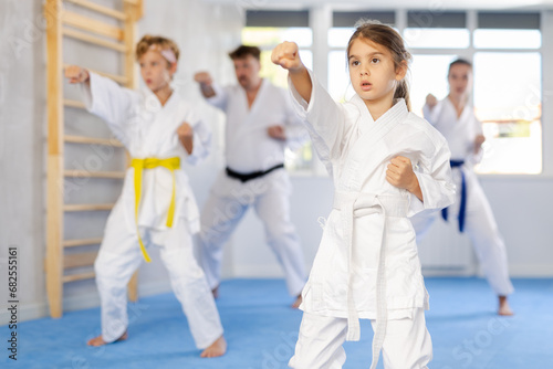 In gym, family of four repeats movements of karate card and practicing kicks and punches in unison, is intently preparing for sparring.