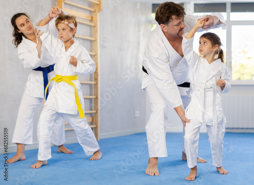 Children with parents practicing judo together on sports mats in gym