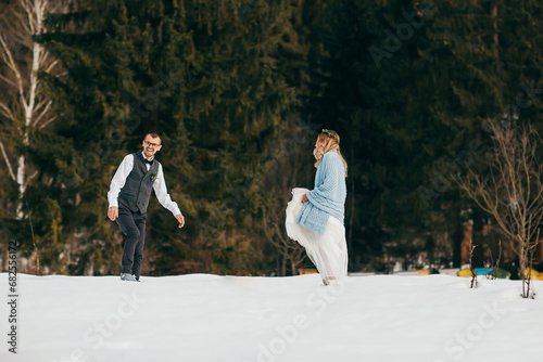 Young couple bride and groom playing in the winter nature on the background of the forest. They run and throw snow. Jump. Have a good time laughing. The concept of a winter wedding in the mountains