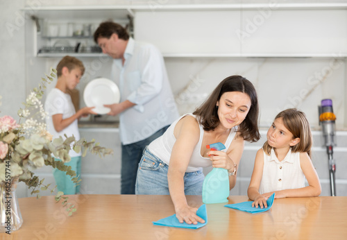 Joyful family with two children doing cleaning in kitchen in apartment