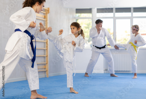 Focused preteen girl in white kimono practicing karate kicking techniques during sparring with mother. Sports family activity concept..