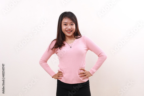 Confident cheerful pretty young asian girl standing while looking at the camera confidently. Hand on waist. Isolated on white