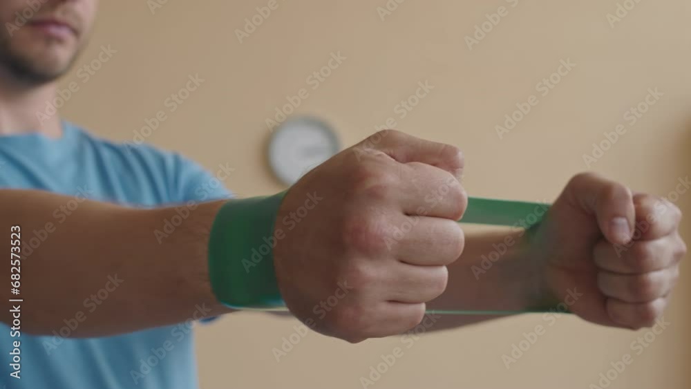 Close up shot of hands of male patient pulling resistance band while doing rehabilitation exercise under control of female doctor in physiotherapy clinic Close up shot of hands of male patient pulling resistance band while doing rehabilitation exercise under control of female doctor in physiotherapy clinic