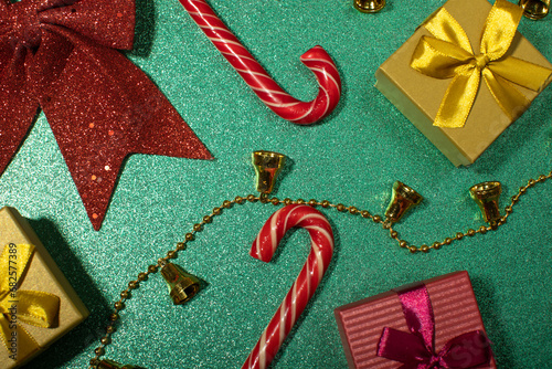 different gift boxes, hristmas bells, candy canes on green glint background top veiw, horizontal photo photo