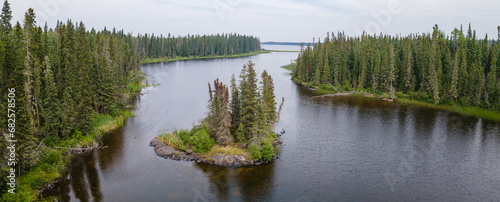 An aerial view taken from treetop level and looking down at a river that cuts through a dense forest of spruce trees. A small rocky island is near the center of the image. 