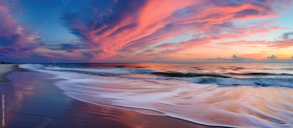 In the midst of summer, with the sky ablaze in hues of pink and orange, the tranquil beach became a canvas for nature's artistry, as water and clouds met in a harmonious dance, while the line where