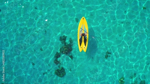 Aerial top down view woman paddle yellow sup. Crystal blue sea water coral reef. Outdoor active sport lifestyle travel on summer holiday vacation. Natural background. Drone shot