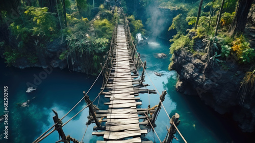 Old suspension bridge across river in jungle, perspective view of hanging vintage wooden footbridge. Scenery of tropical forest and water. Concept of travel, adventure, nature