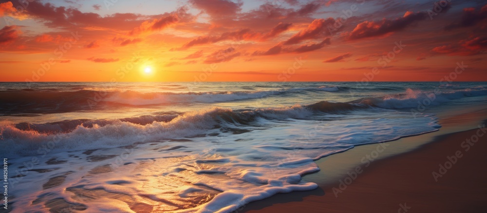 As the sun sets on the horizon, painting the sky in shades of orange and red, the shimmering waves crash onto the sandy beach, creating a breathtaking panorama in the summer night; a stunning display
