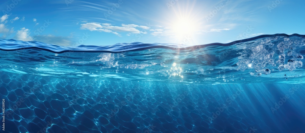 Fototapeta premium As the sun's radiant light illuminates the clear, deep blue waters of the ocean, a mesmerizing abstract world unfolds before their eyes; the rippling texture of the sea creates a cool and refreshing