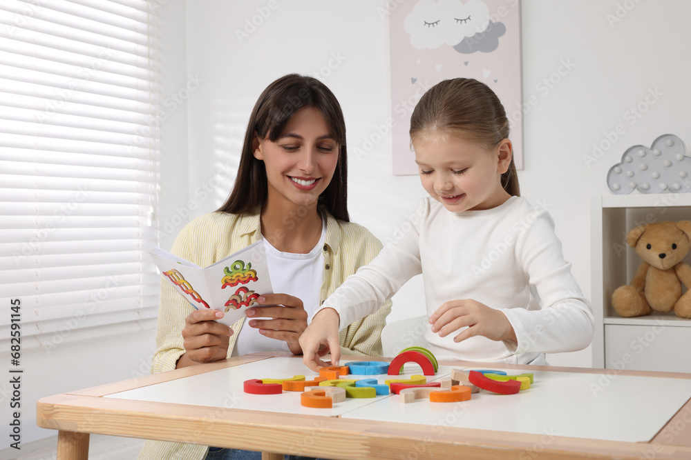 Motor skills development. Mother helping her daughter to play with colorful wooden arcs at white table in room