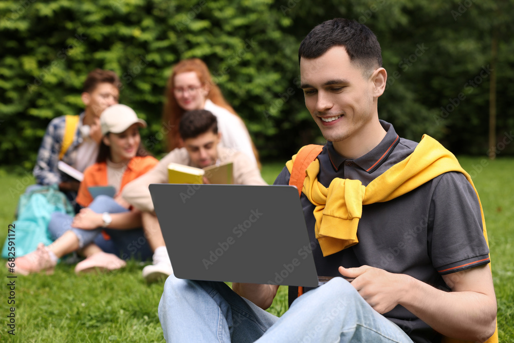 Students learning together in park. Happy young man working with laptop on green grass, selective focus Students learning together in park. Happy young man working with laptop on green grass, selective focus