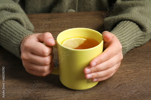 Woman holding mug of tea at wooden table, closeup