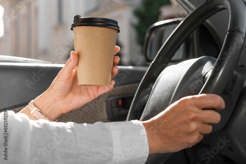 Coffee to go. Woman with paper cup of drink driving her car, closeup