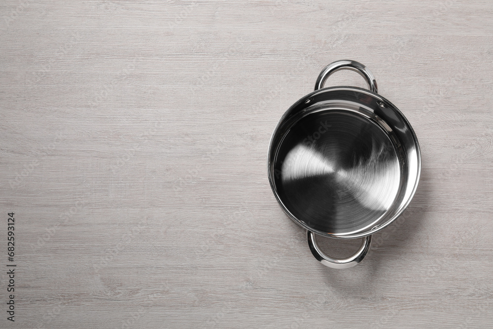 Empty steel pot on light wooden table, top view. Space for text