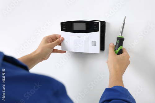 Man installing home security alarm system on white wall indoors, closeup photo