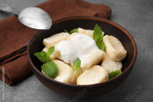 Bowl of tasty lazy dumplings with sour cream and mint leaves on brown table