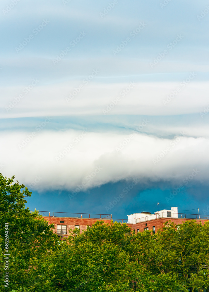 Rolling Clouds Over Urban Greenery and Rooftops. White cloud on blue pre-storm sky in New York, USA, background, weather