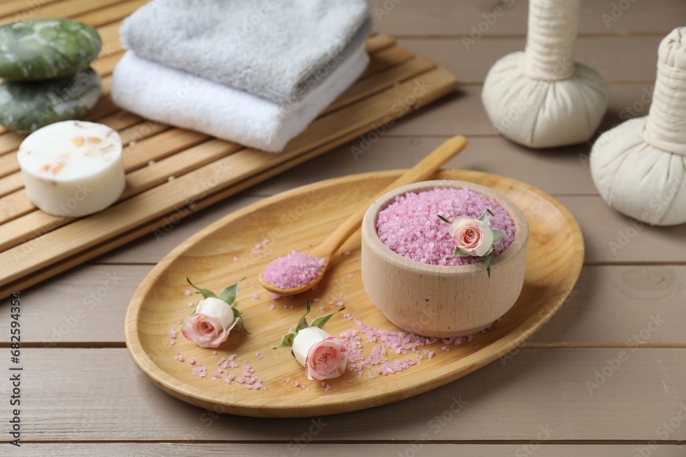 Bowl of pink sea salt, roses, herbal massage bags and towels on wooden table Bowl of pink sea salt, roses, herbal massage bags and towels on wooden table