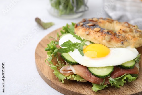 Tasty bagel with cured ham, egg, cucumber and salad mix on light table, closeup. Space for text
